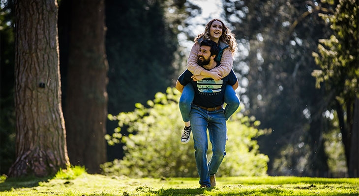 A man carrying a woman on his back in a park, enjoying a fun and playful moment together.